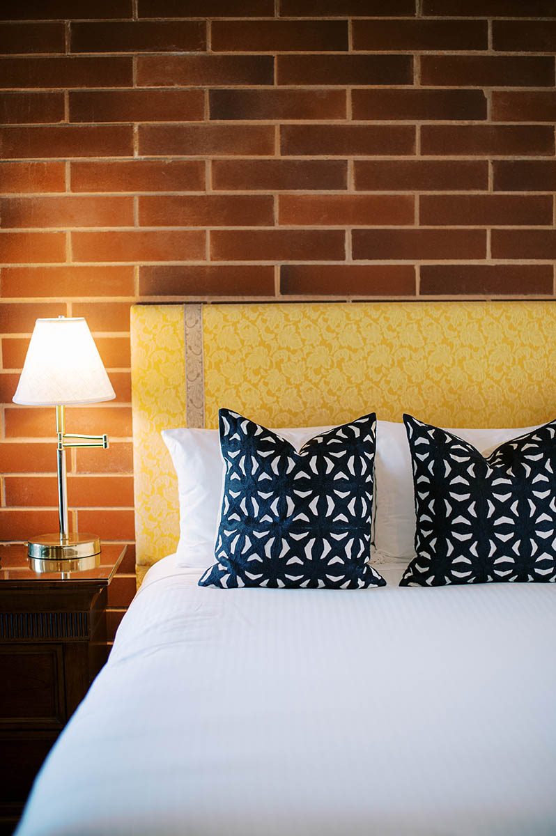 King bed in an Embarcadero Building guest room at Napa River Inn with a yellow upholstered headboard against an exposed red brick wall.