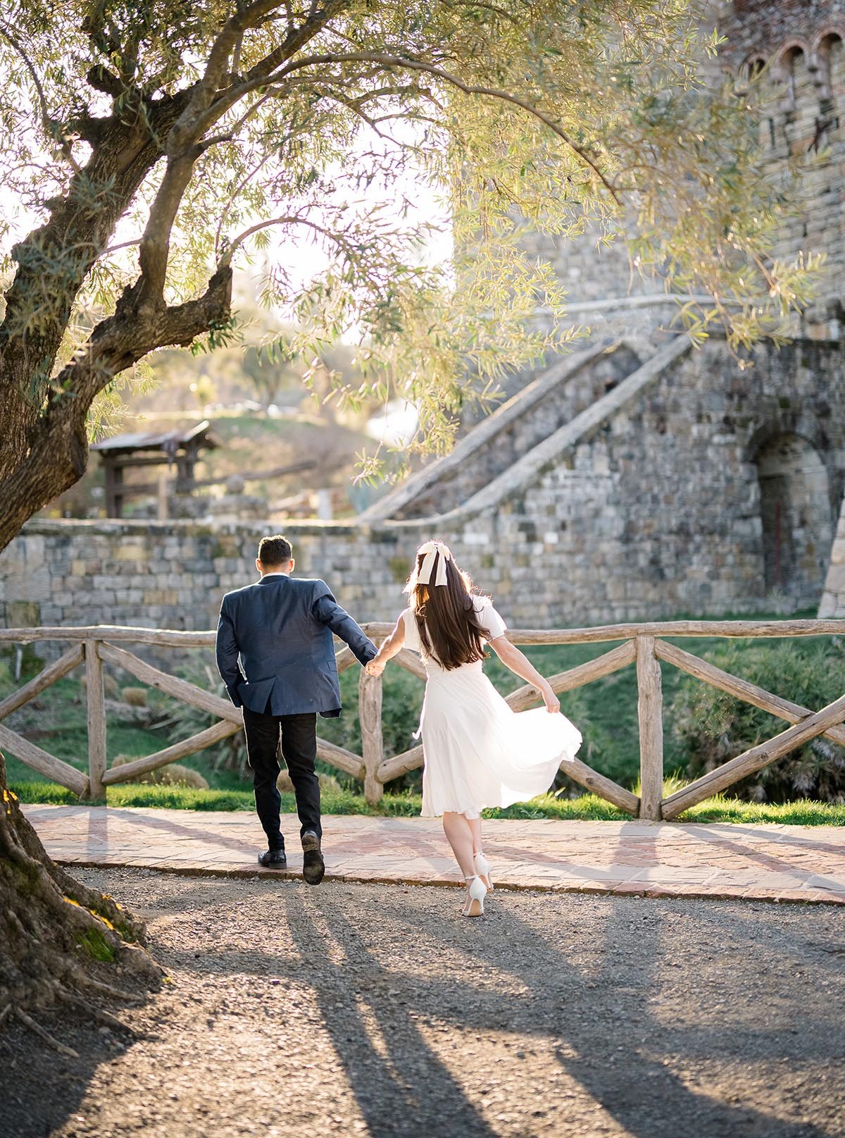 A couple in semi-formal attire walking hand-in-hand through the grounds of a Napa Valley winery castle at golden hour, taken for a Napa River Inn engagement and wedding events feature.