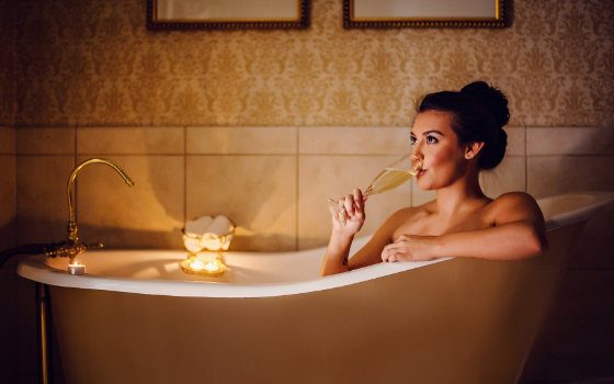 A woman in a soaking tub at Napa River Inn sipping champagne by candlelight, part of the hotel’s Romance Package amenities.